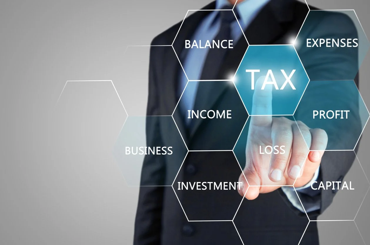 A person in a business suit touching a virtual hexagon labeled 'TAX' with other related terms like 'BALANCE,' 'EXPENSES,' 'INCOME,' 'PROFIT,' and 'LOSS' surrounding it.