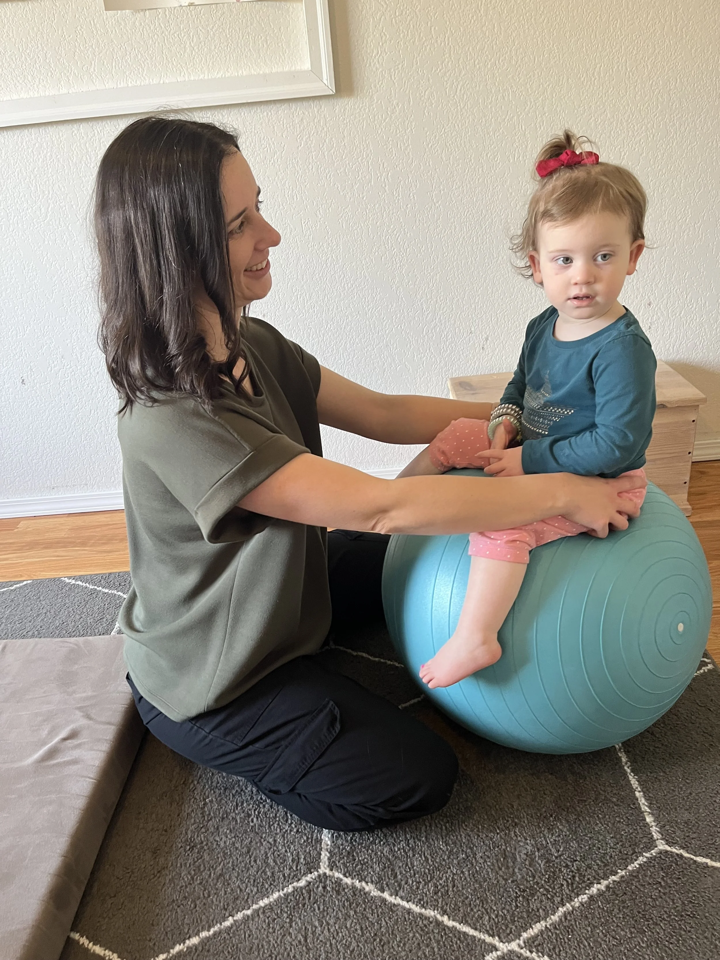An occupational therapist supporting a toddler, who is sitting on a therapy ball.