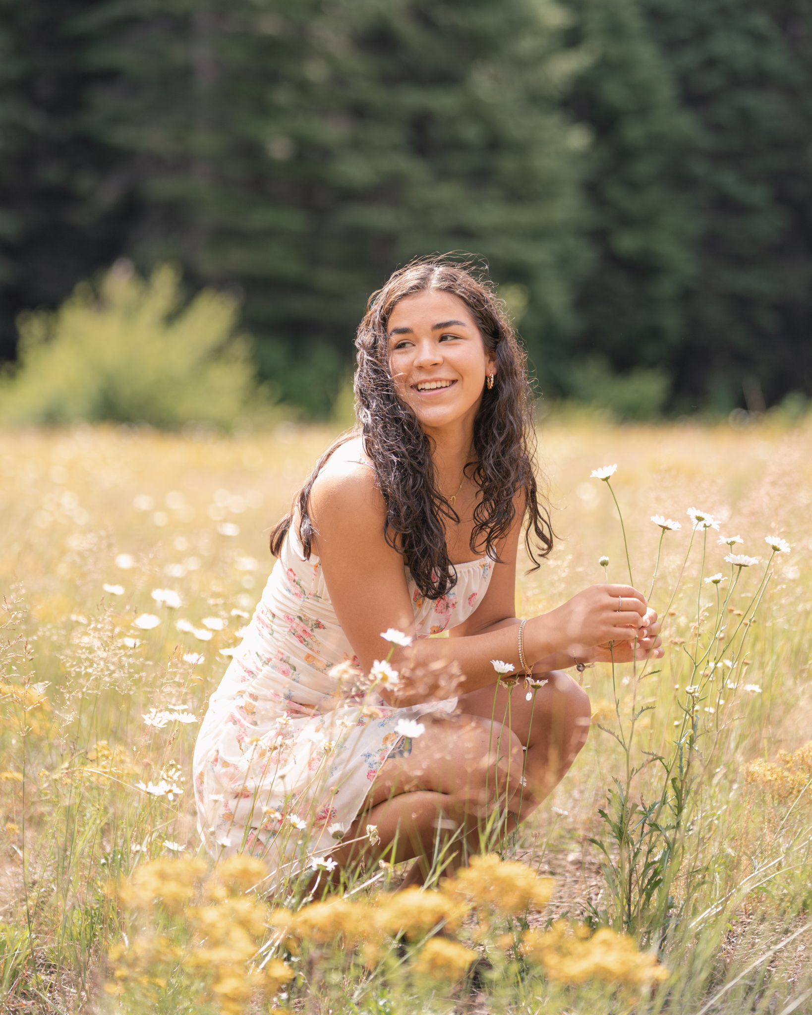Woman squatted down in a floral dress in a flower field smiling