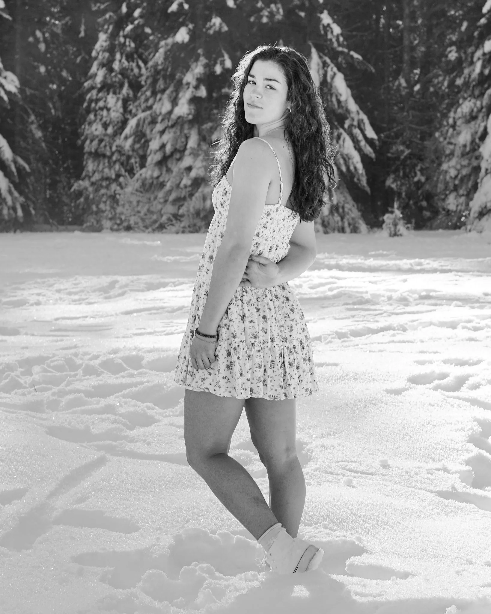 A young woman with curly hair standing in a snow-covered landscape with trees in the background.