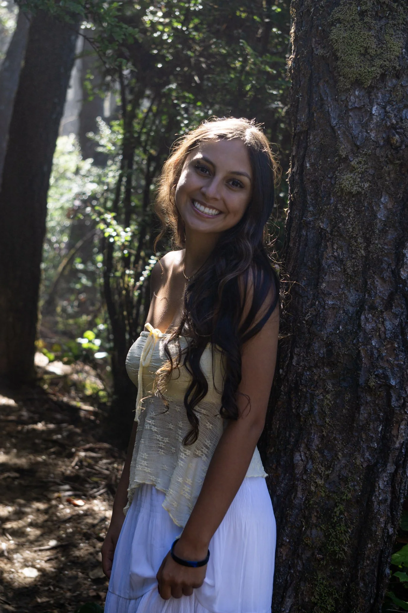 high school senior in a skirt and top smiling and leaning against a tree