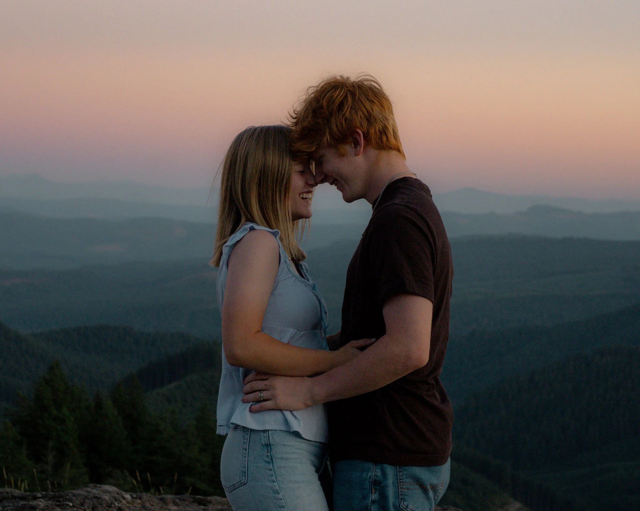 Couple standing on mountain at sunset with foreheads touching