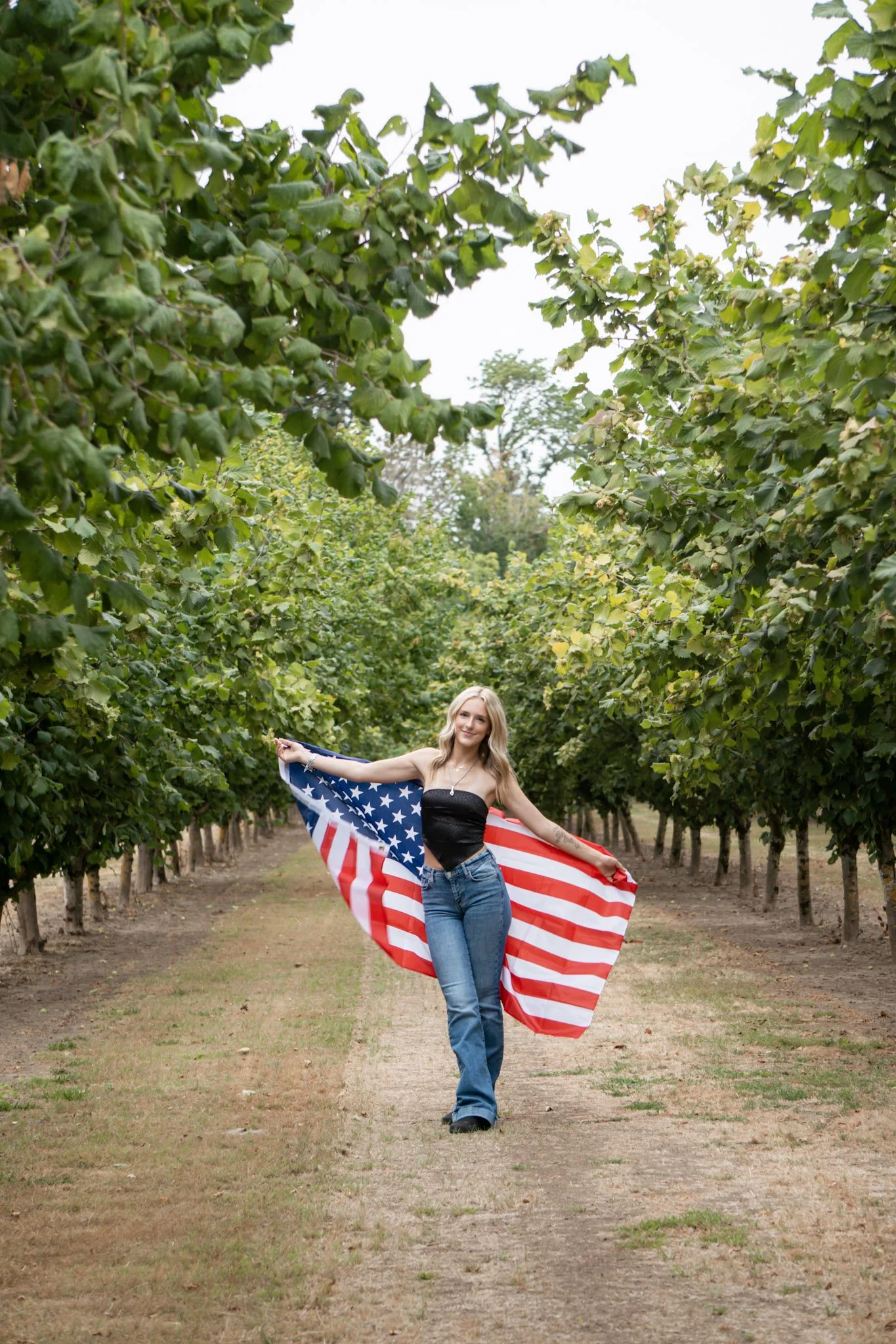 A young woman posing in a vineyard holding an American flag.