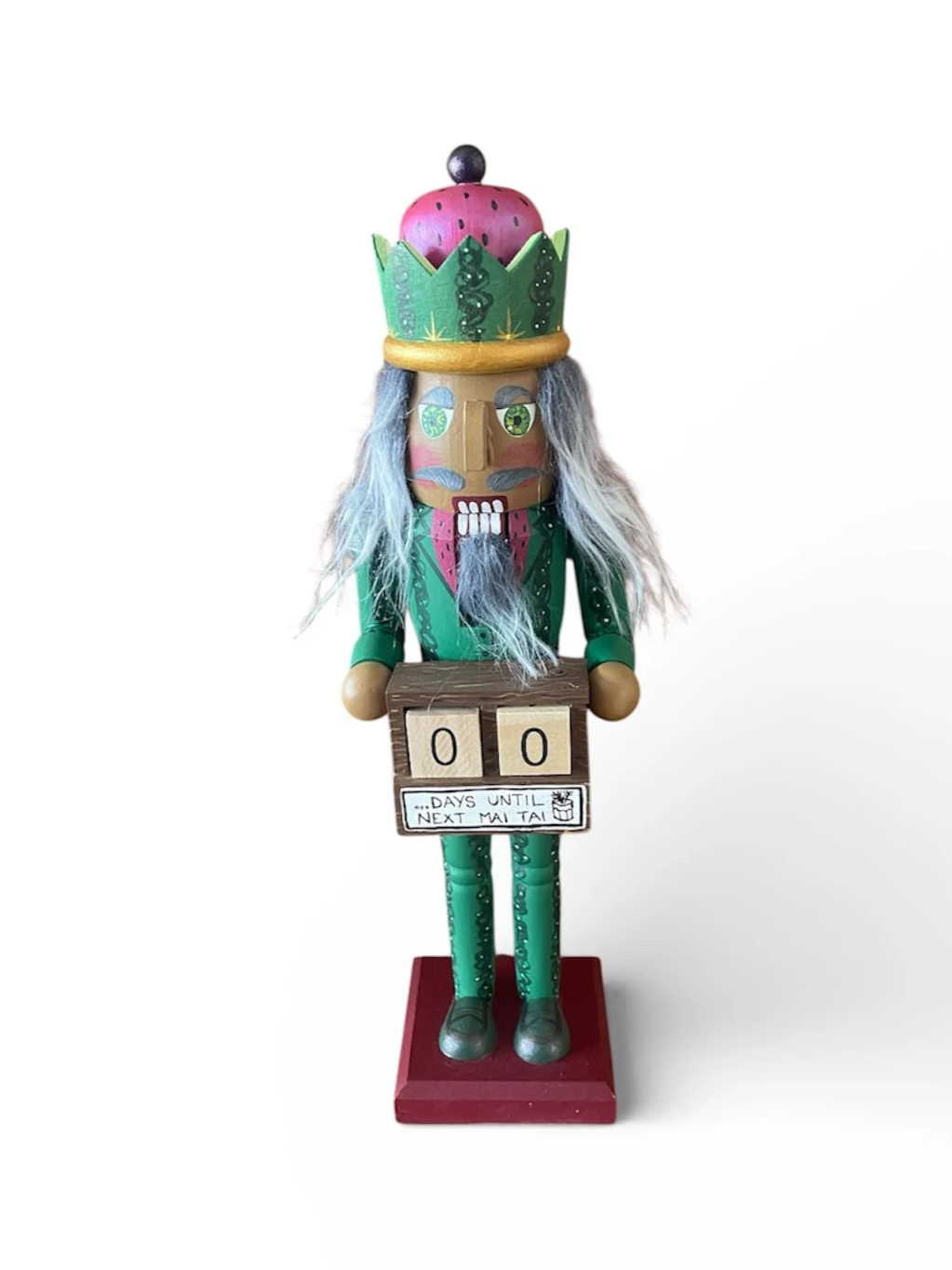 Wooden nutcracker figurine with a strawberry-themed crown, long gray hair, and a pink beard, holding a sign that reads '0 days until next Mai Tai' on a red base with a plain white background.
