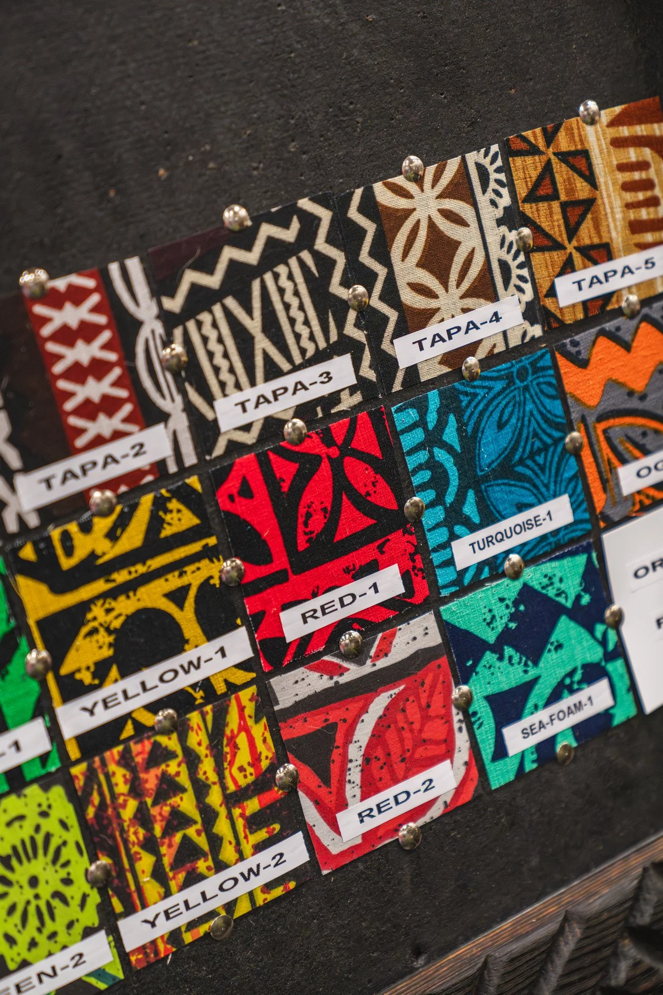 Colorful fabric samples with tribal patterns pinned on a display board, labeled with color names and sample numbers.