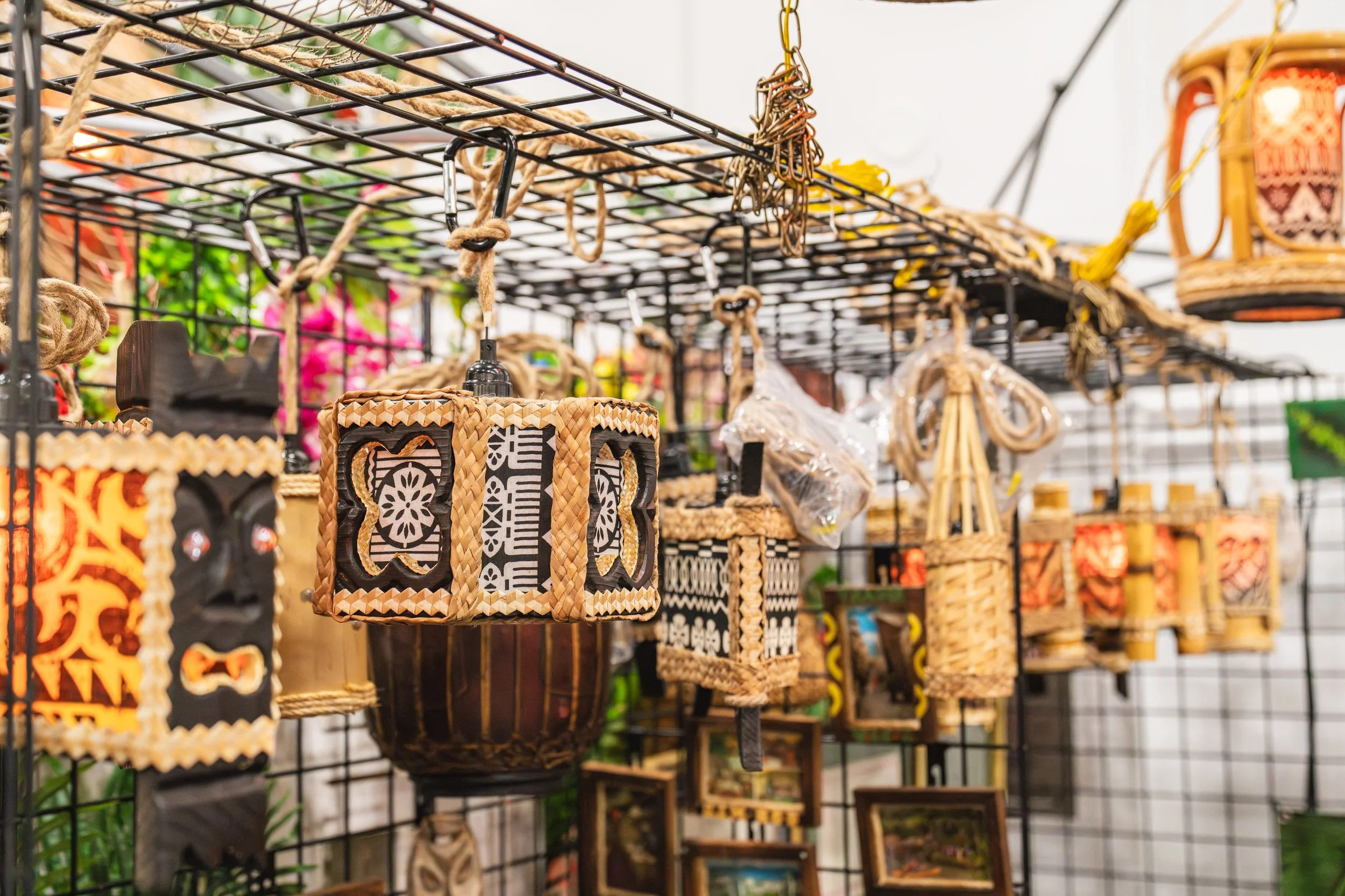 Wicker and wooden lanterns and decor hanging on a black metal display grid at a market or store.
