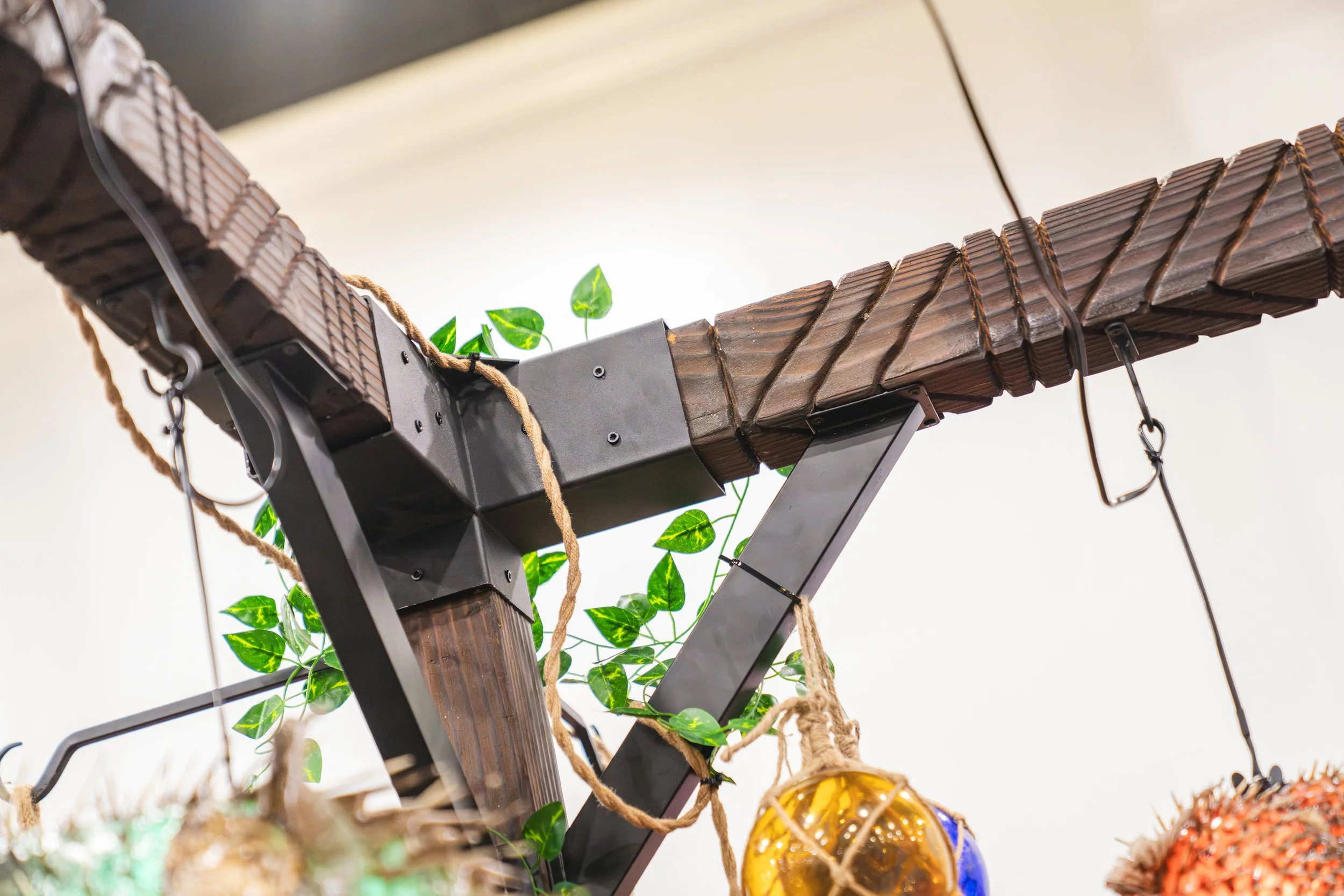 Close-up of a modern ceiling fixture with wooden slats, green artificial vines, and hanging decorative spherical objects.