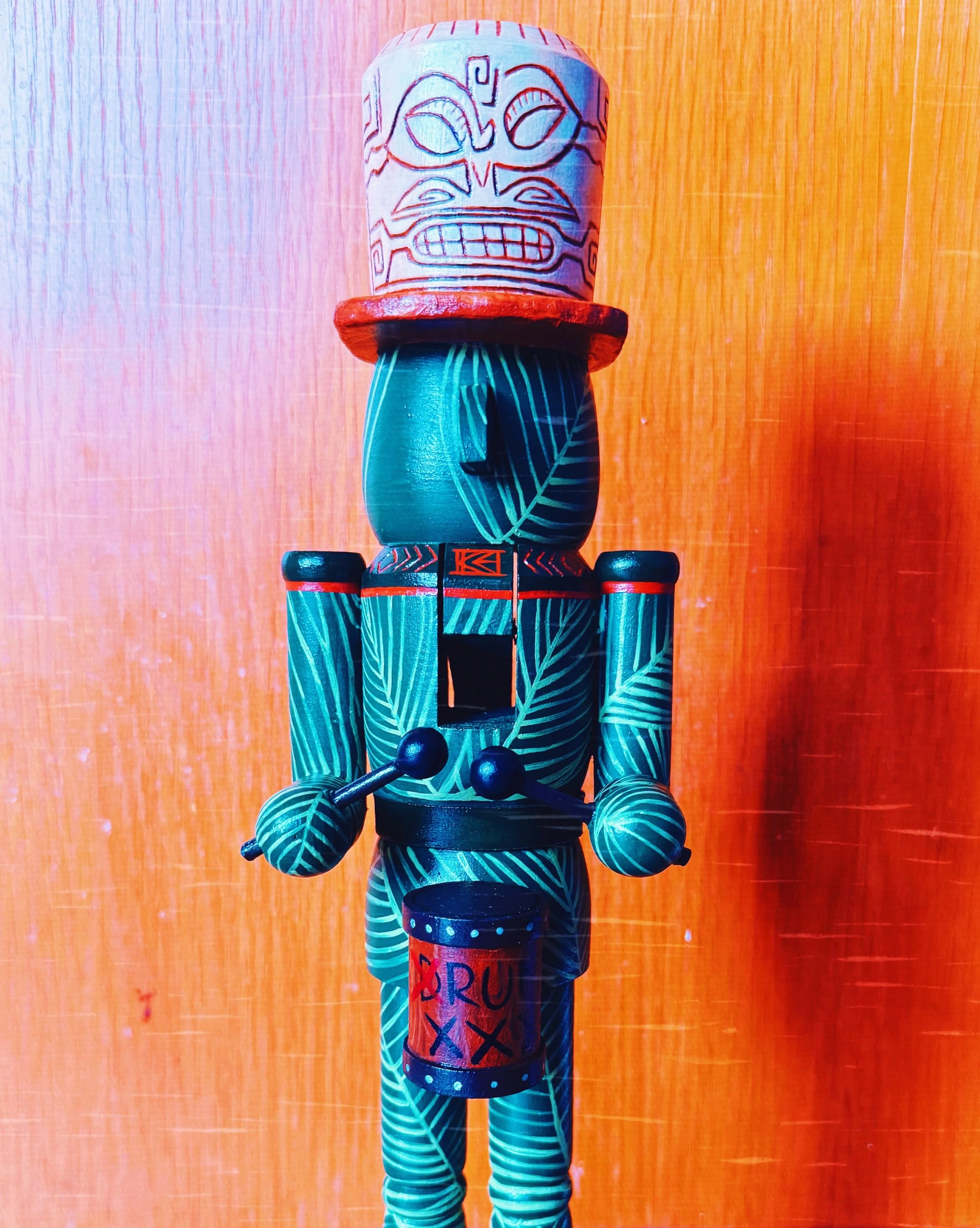 Colorful wooden doll with a painted face, wearing a red hat and blue striped clothing, standing against a wooden background.