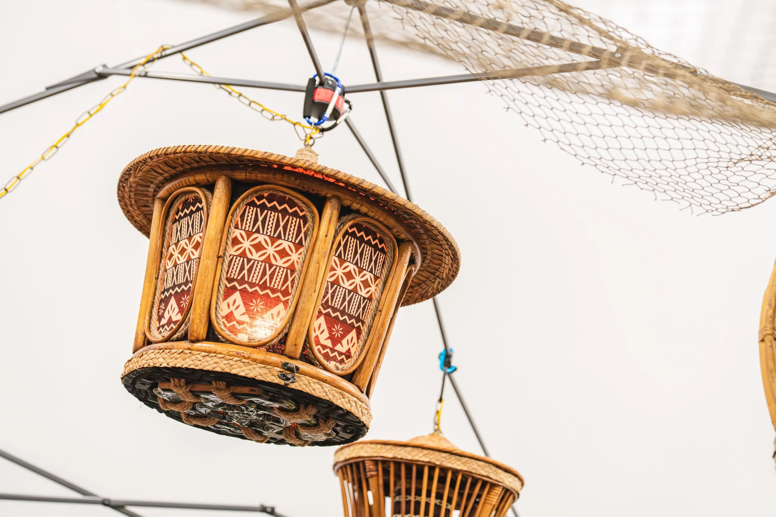 Hanging lantern made of woven wood and patterned fabric, suspended by metal frame and chains.
