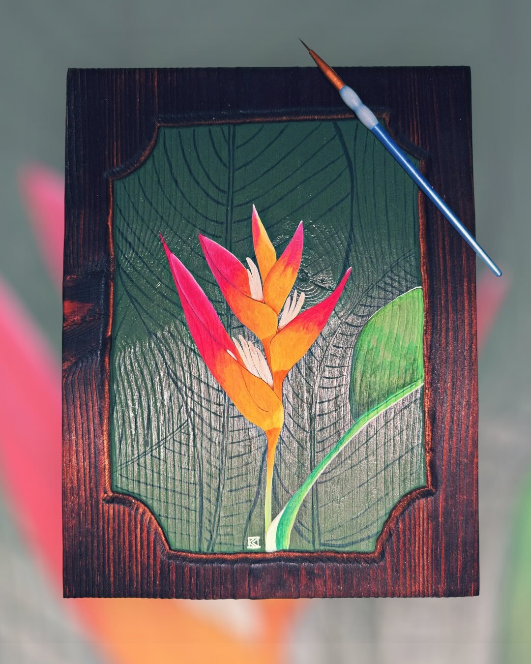 Painting of tropical flowers and leaves on a wooden panel with a paintbrush resting on top.