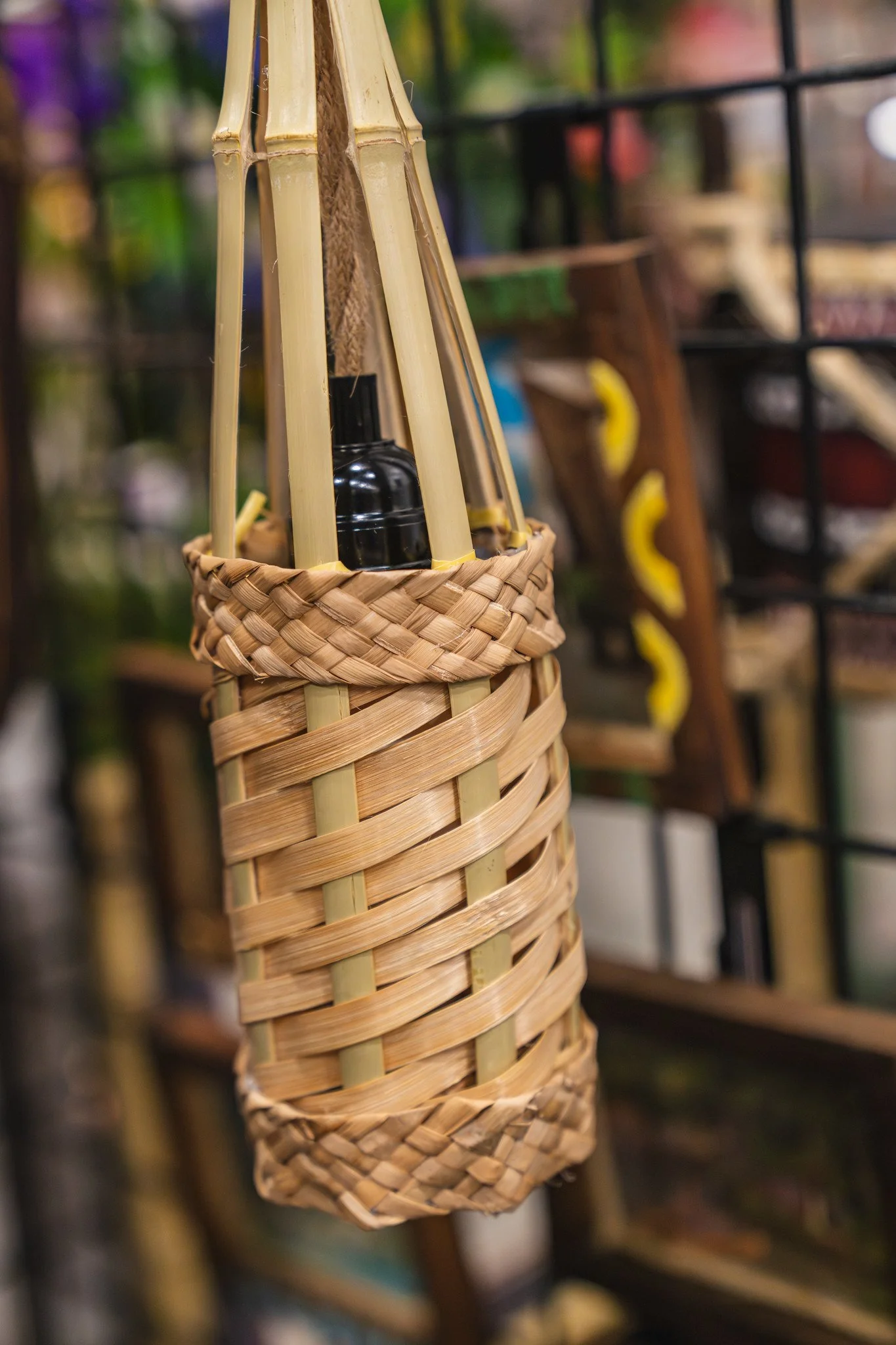 Close-up of a woven basket with bamboo and a small black glass bottle inside it, against a blurred background of more baskets and shelves.
