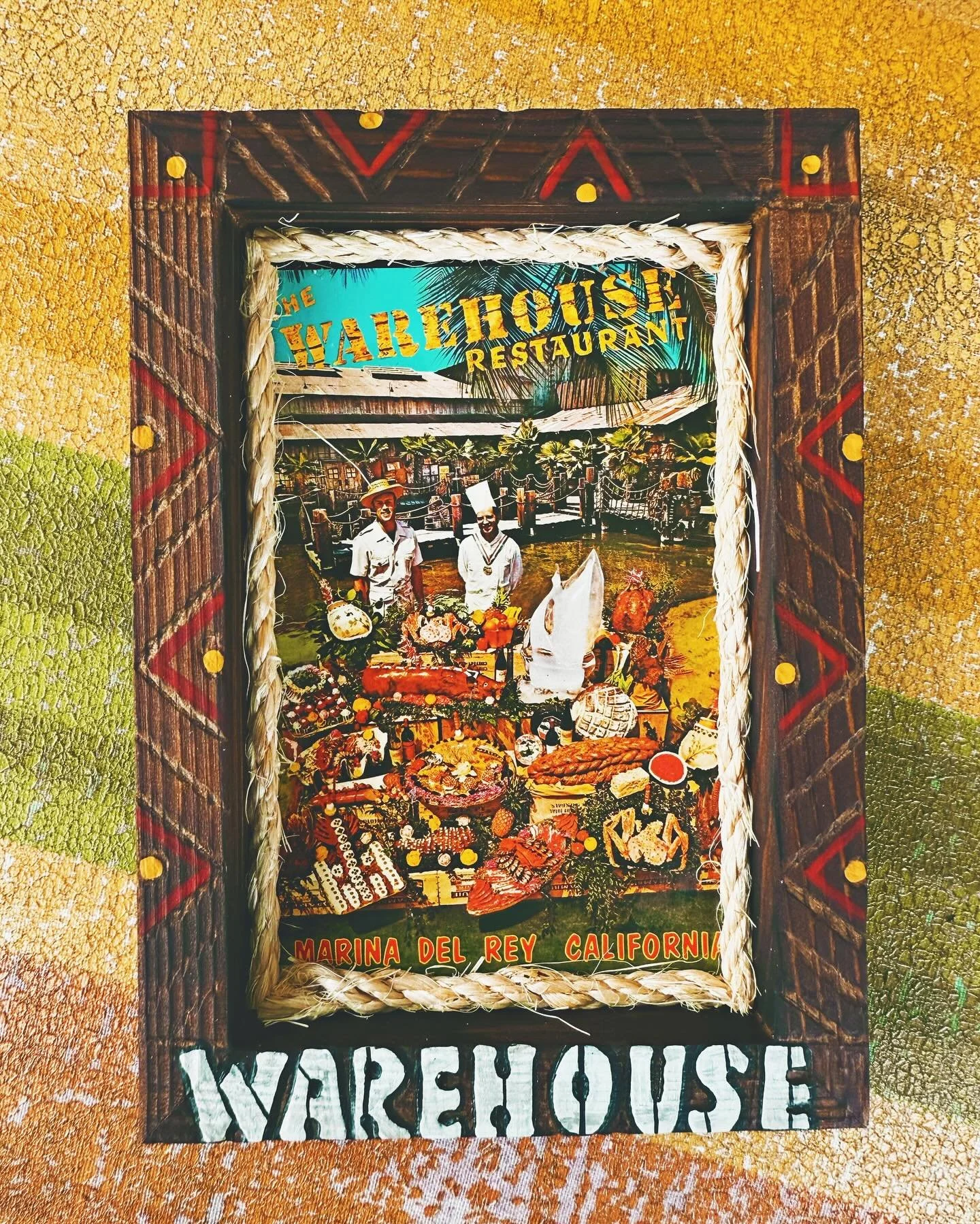 Colorful sign advertising the Warehouse Restaurant in Marina del Rey, California, featuring images of food, two people, and decorative elements with warm colors and bold text.