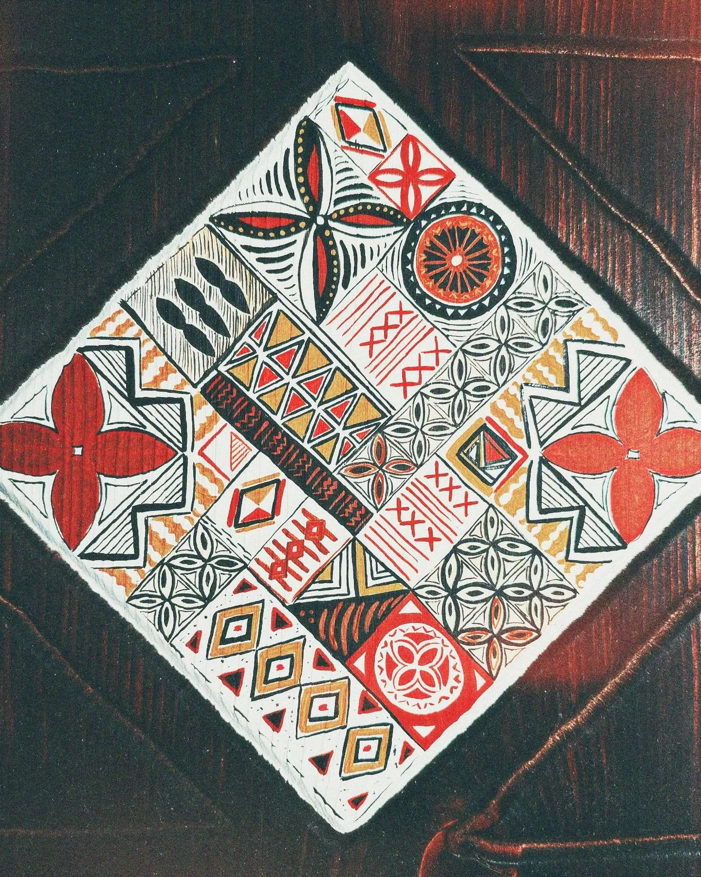 Close-up of a decorative cloth with geometric patterns in red, black, white, and gold colors, on a dark wooden surface.
