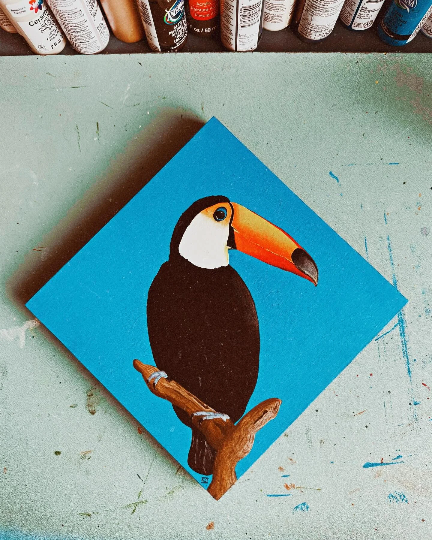 A painting of a toucan bird on a branch, with a bright blue background.