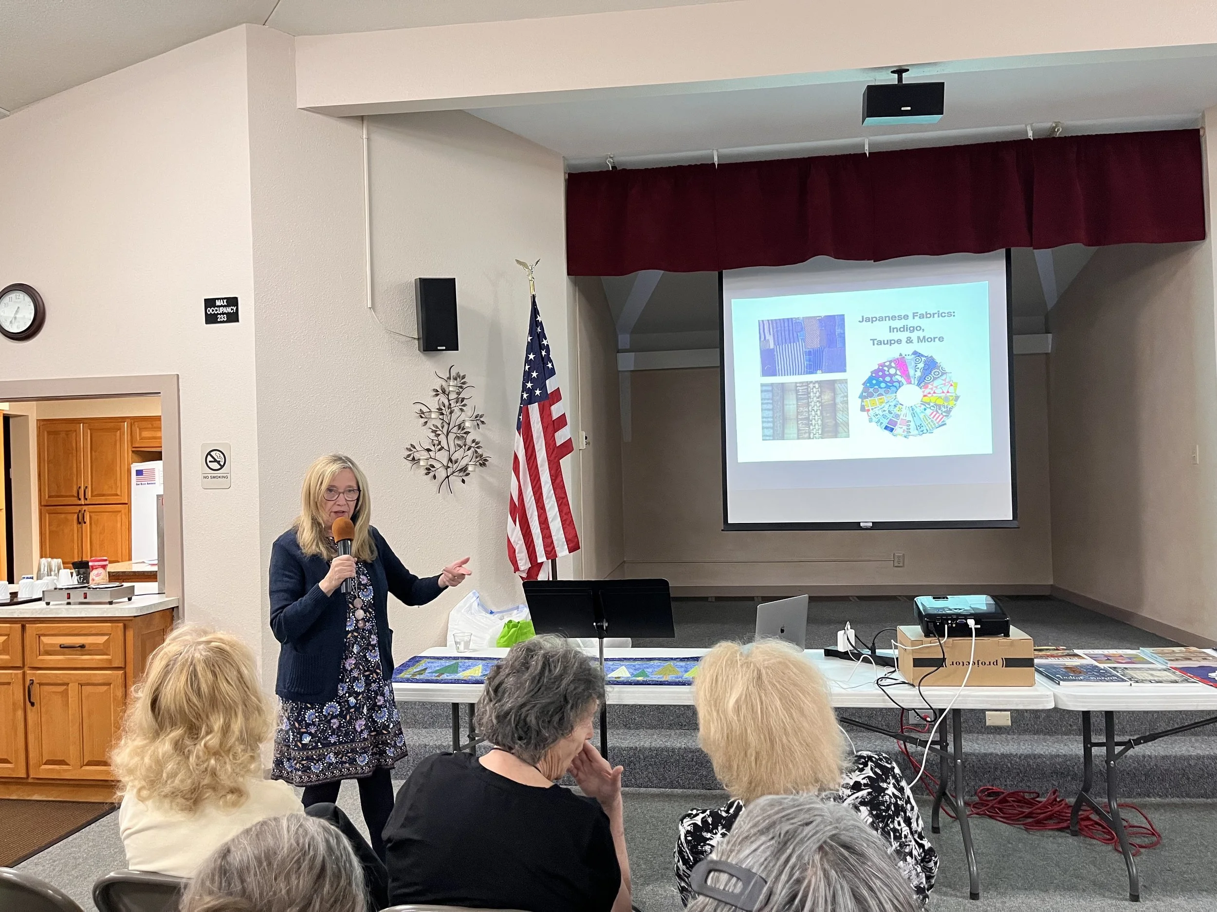 A woman stands in front of a projector screen presenting about Japanese fabrics and dyeing techniques.