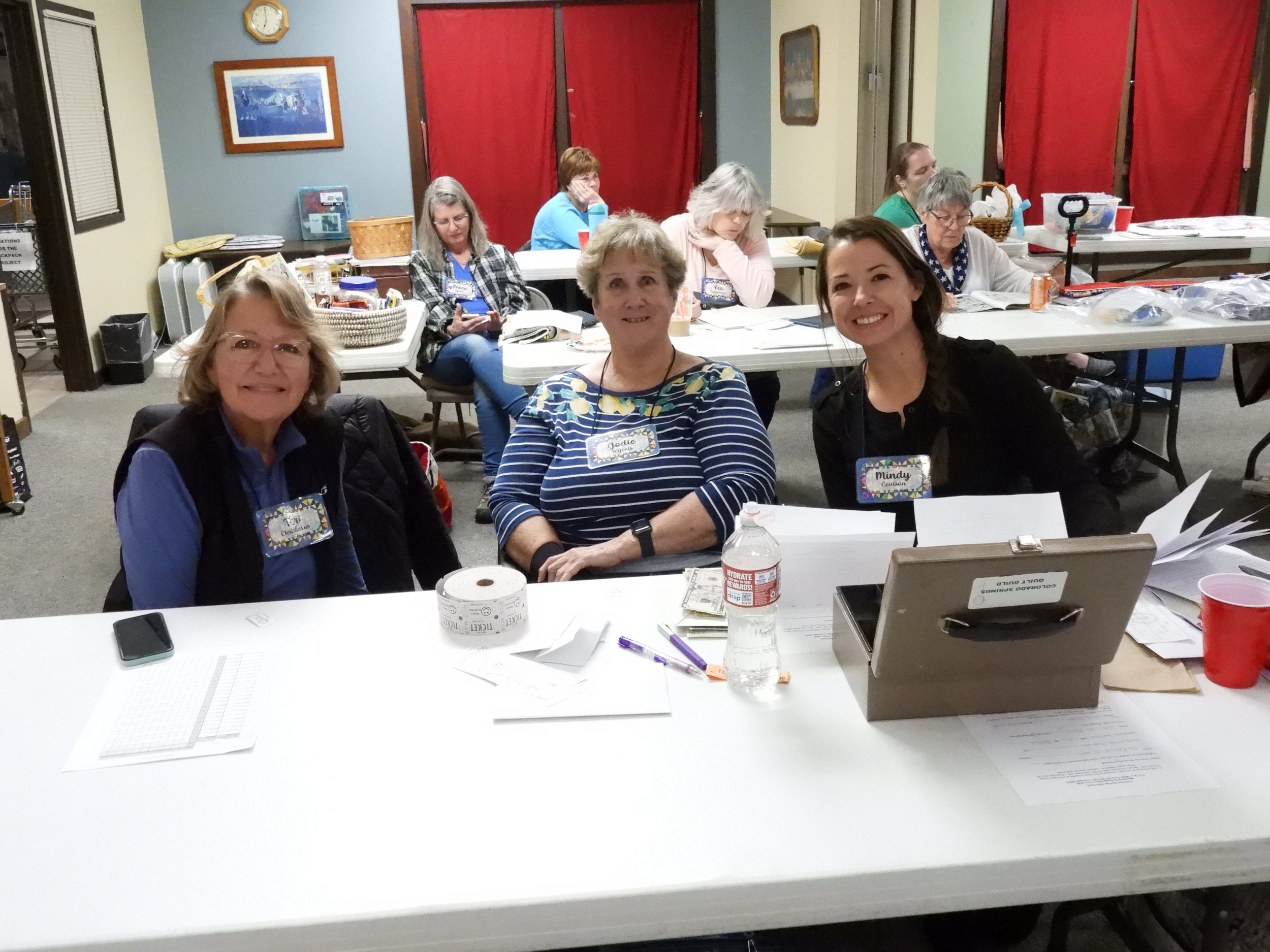 Three women sit at the member registration table at a monthly guild meeting.
