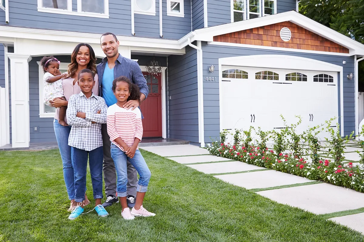 Family of five standing on front lawn of blue house with red door, smiling