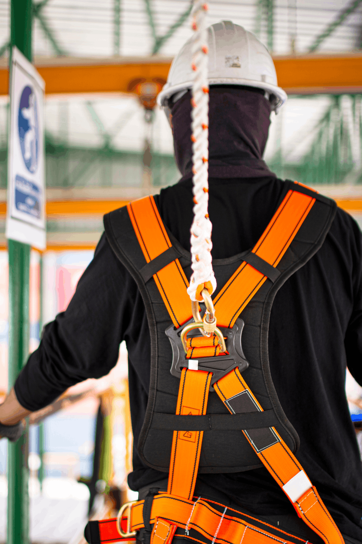 A person wearing a hard hat and safety harness stands on a platform, with shipping containers visible in the background.