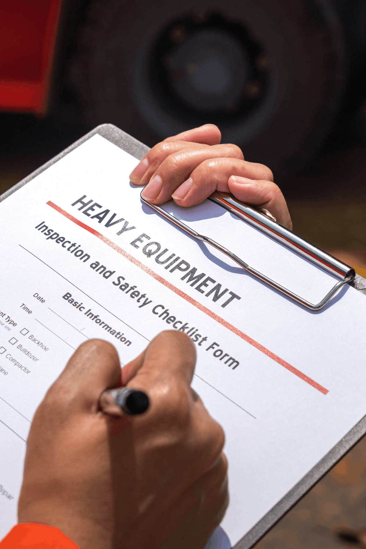 A person is filling out a heavy equipment inspection and safety checklist form on a clipboard with a pen.
