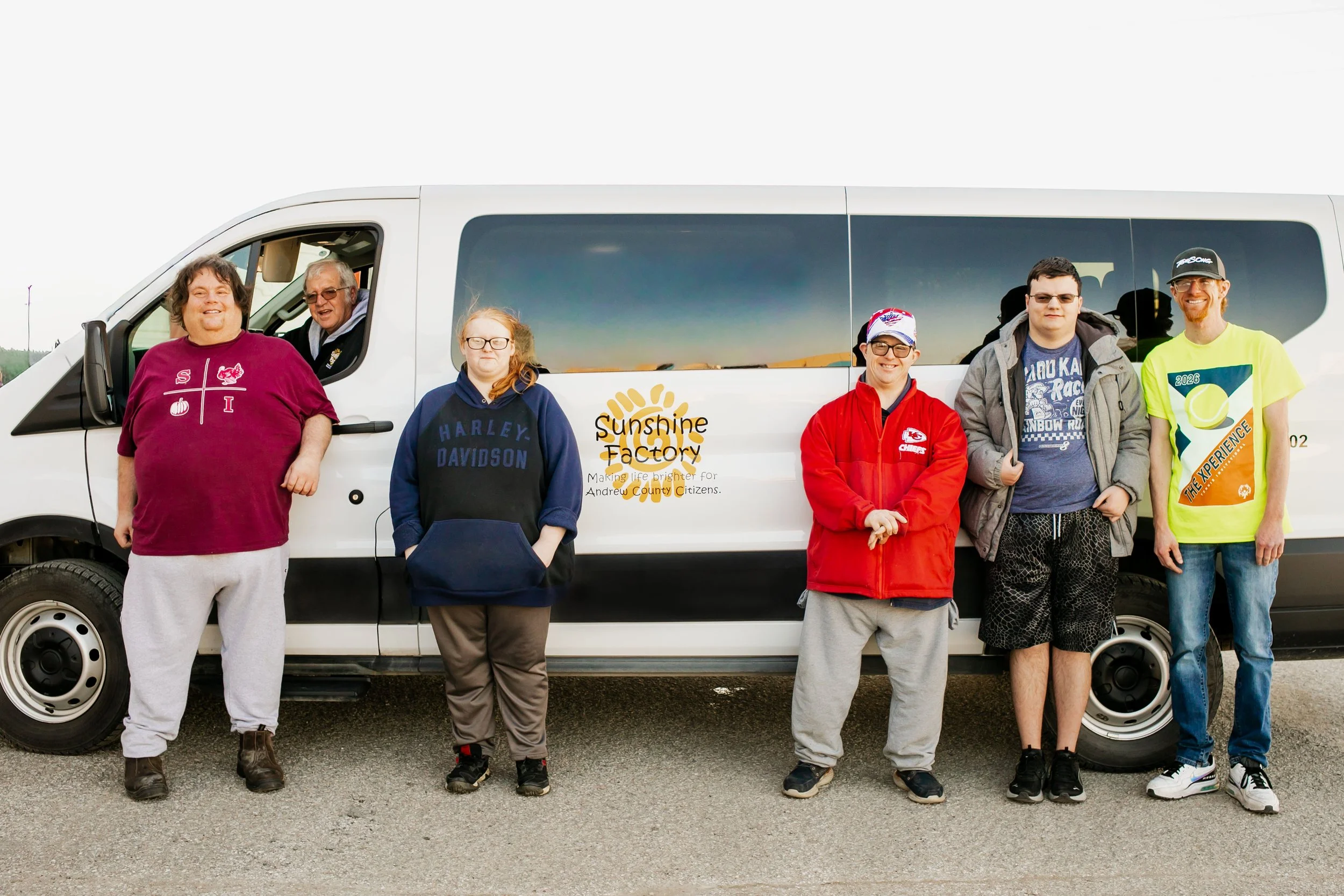 4 people smiling standing in front of white sunshine factory bus