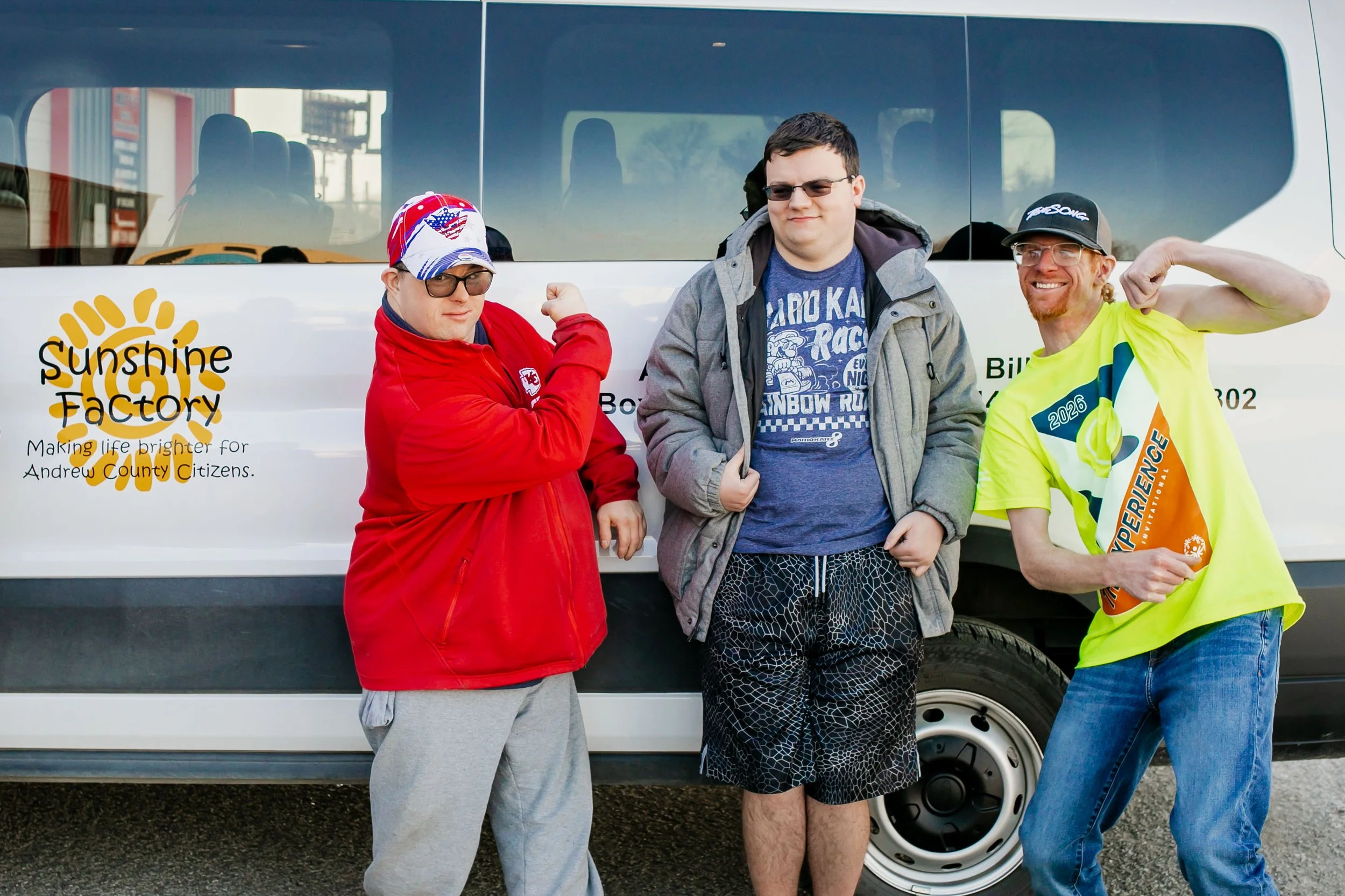 Three middle aged students flexing in front of the sunshine factory bus