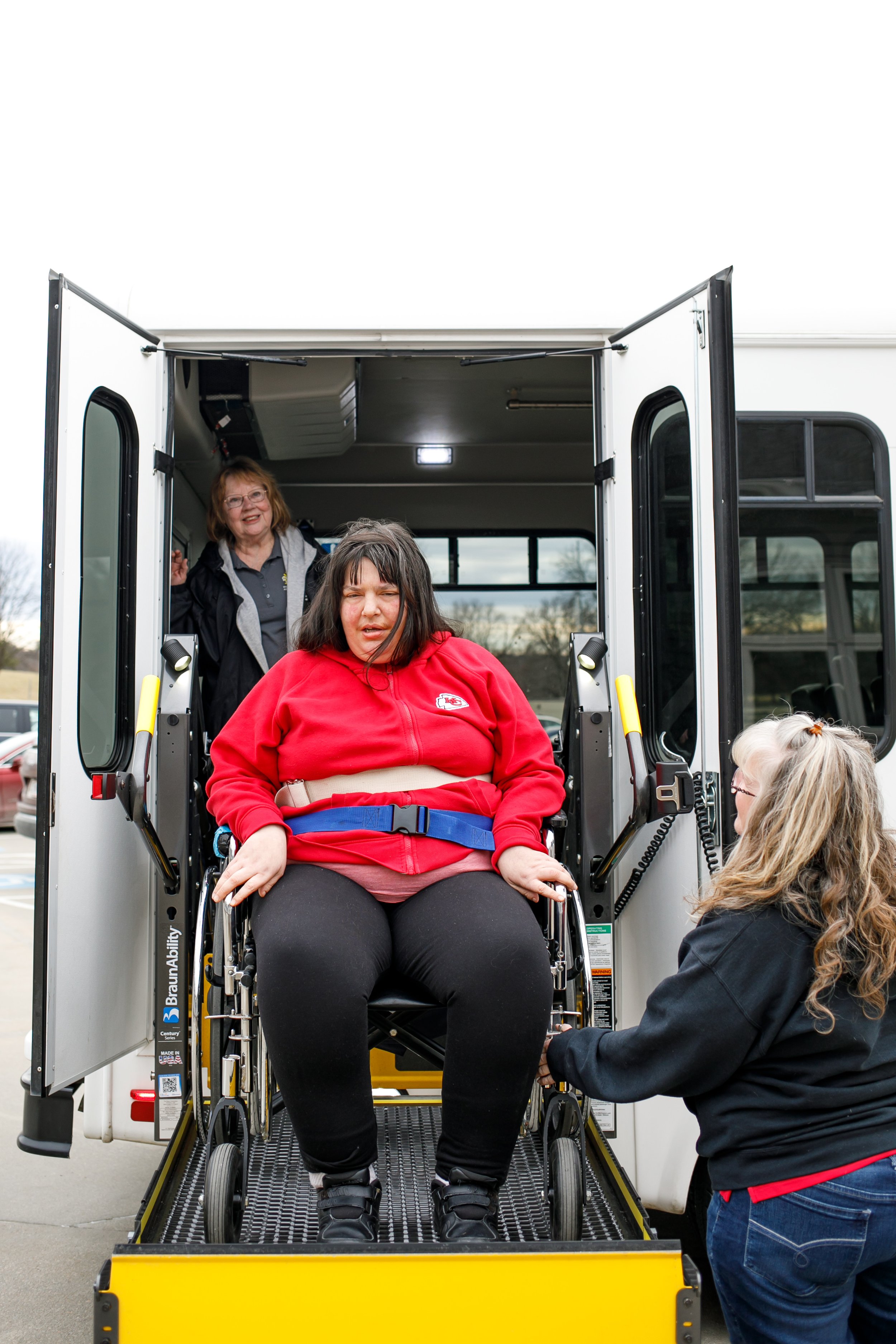 Woman in red jacket coming down from wheel chair lift on sunshine factory bus