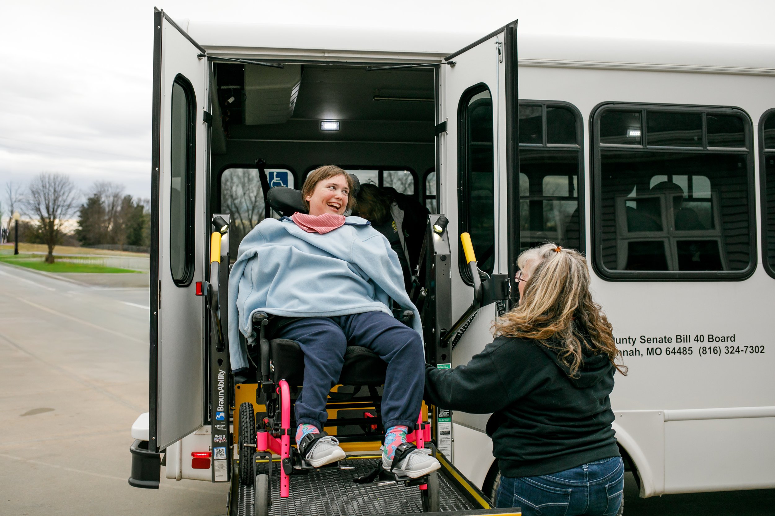 Helping student off wheel chair lift on sunshine factory transportation bus