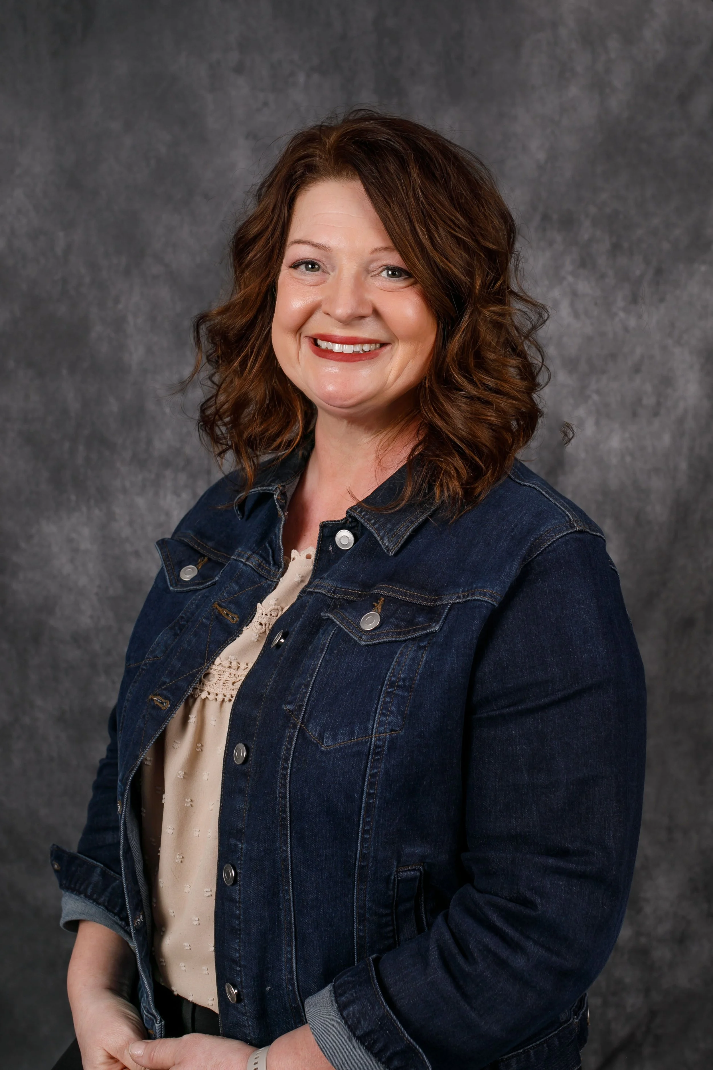 woman smiling wearing blue jean jacket on dark background