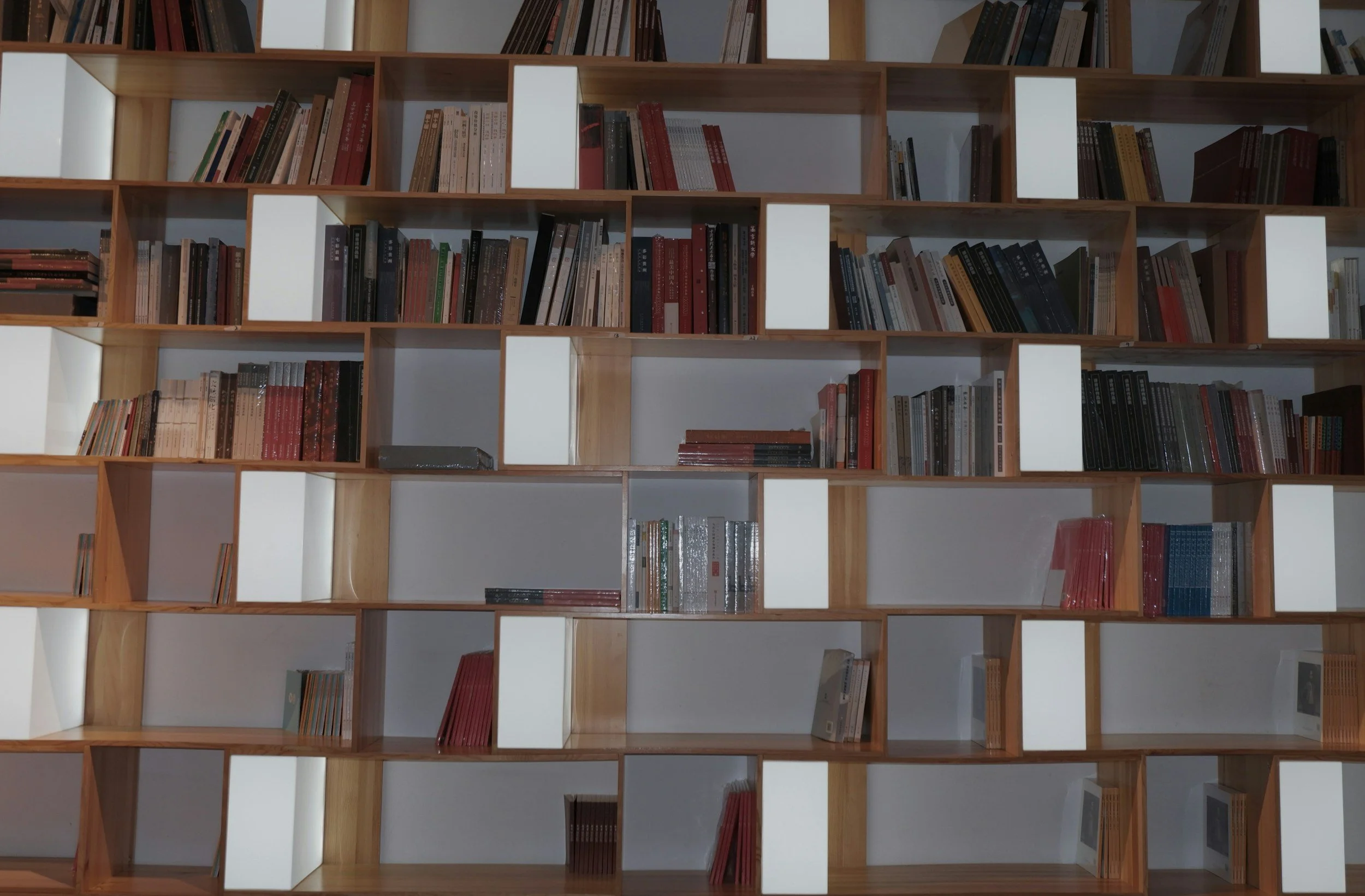 Multiple wooden bookshelves filled with various books, some partially empty, with white display boxes on some shelves.