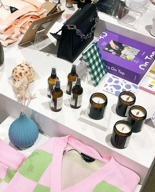 Display of small brown bottles, black candles, and decorative items on a retail table with clothing and books.