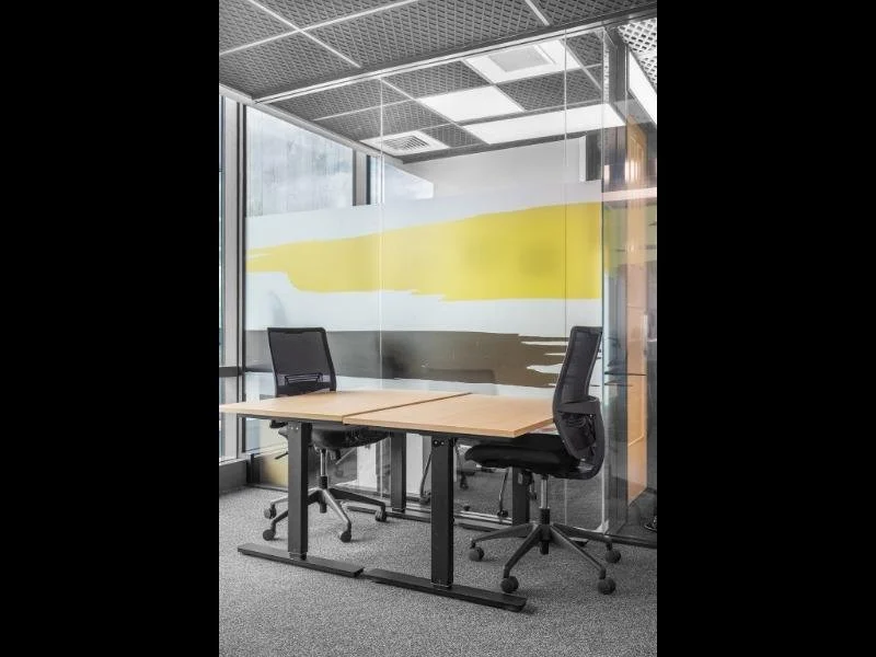 Empty office conference room with a table and two office chairs, glass walls, and ceiling lights.