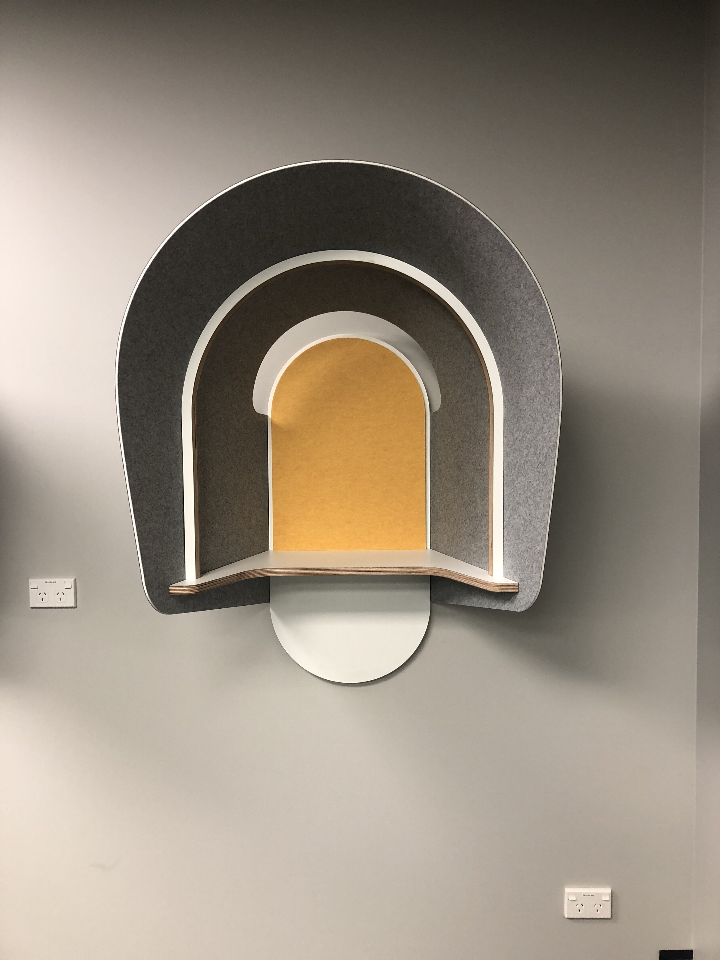 Modern decorative wall shelf with an arch design, featuring a yellow back panel, gray outer shell, white inner border, wood ledge, and a circular base attached to the wall.