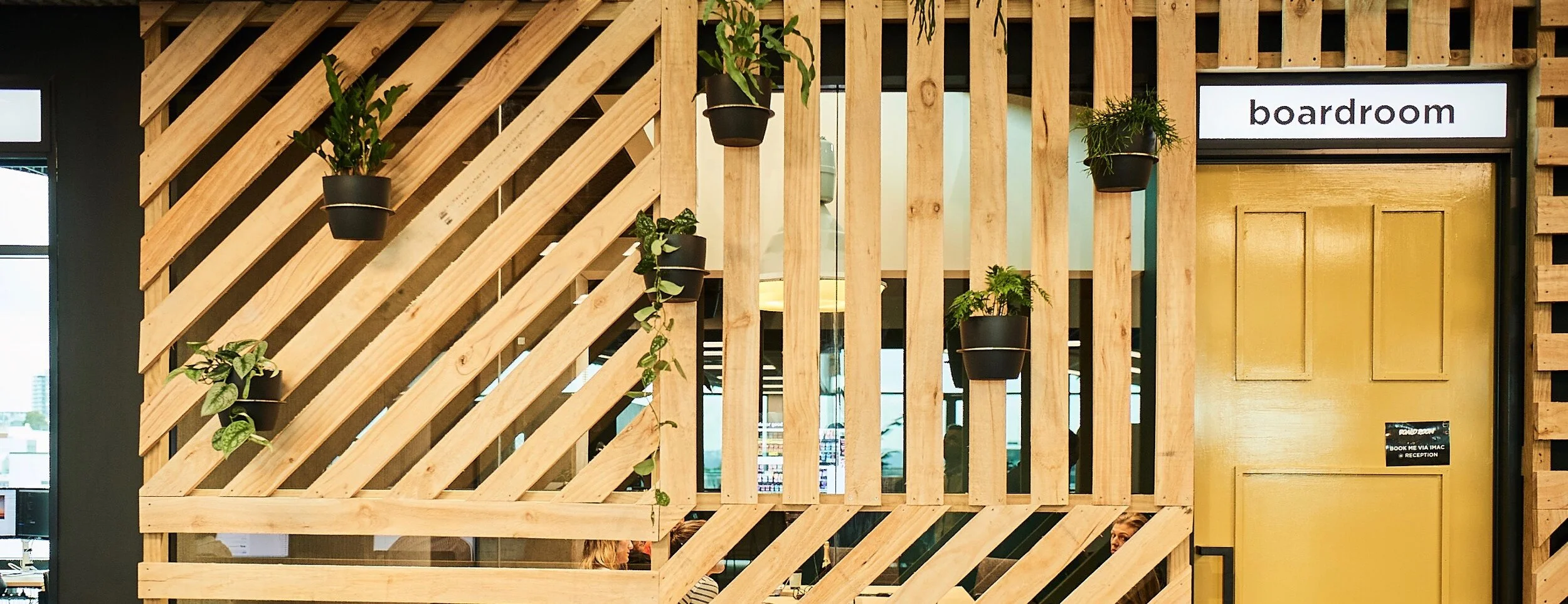 Indoor wooden partition with potted plants and a sign labeled 'boardroom' at an office reception area.