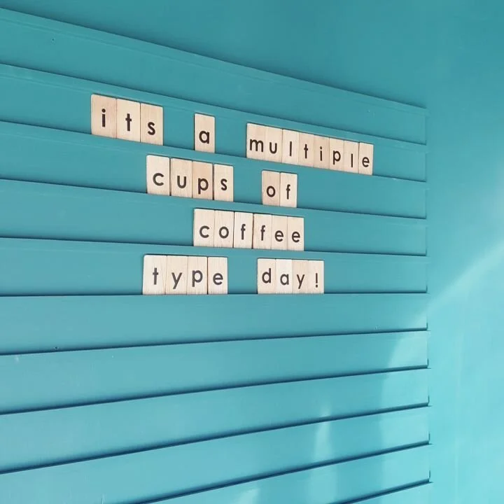 Letter tiles on blue wall spell out: 'It's a multiple cups of coffee type day!'