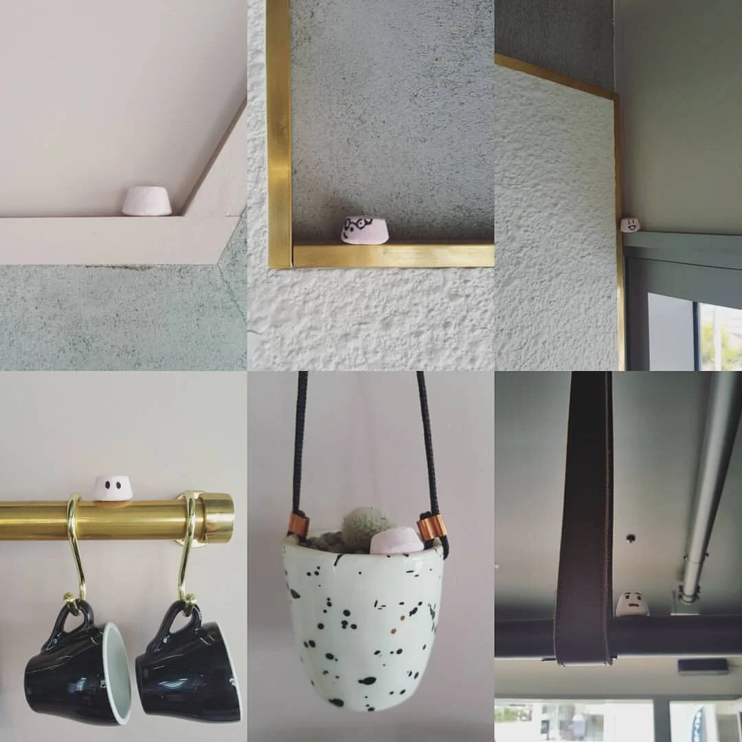 Small decorative objects with faces peeking out from various places, including a corner shelf, wall frames, hanging planters, and hooks in an interior setting.