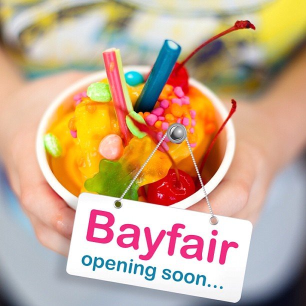 Colorful ice cream served in a cup with sprinkles, candy, and cherries, and a sign saying "Bayfair opening soon..."