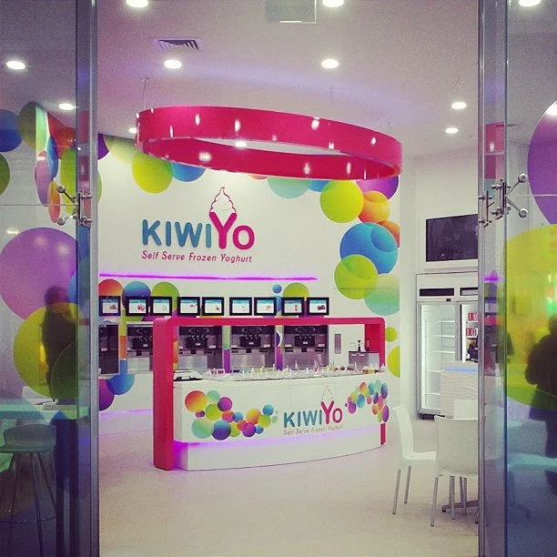 Interior of Kiwi Yo self-serve frozen yogurt shop with colorful decor and ice cream machines.