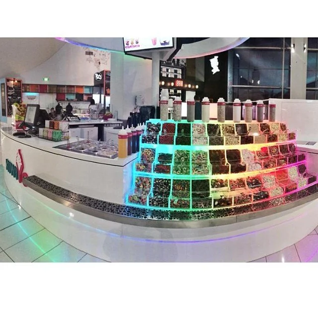 A colorful candy or snack display with bottles and containers arranged in a pyramid shape, illuminated by vibrant neon lights in a modern, spacious interior.