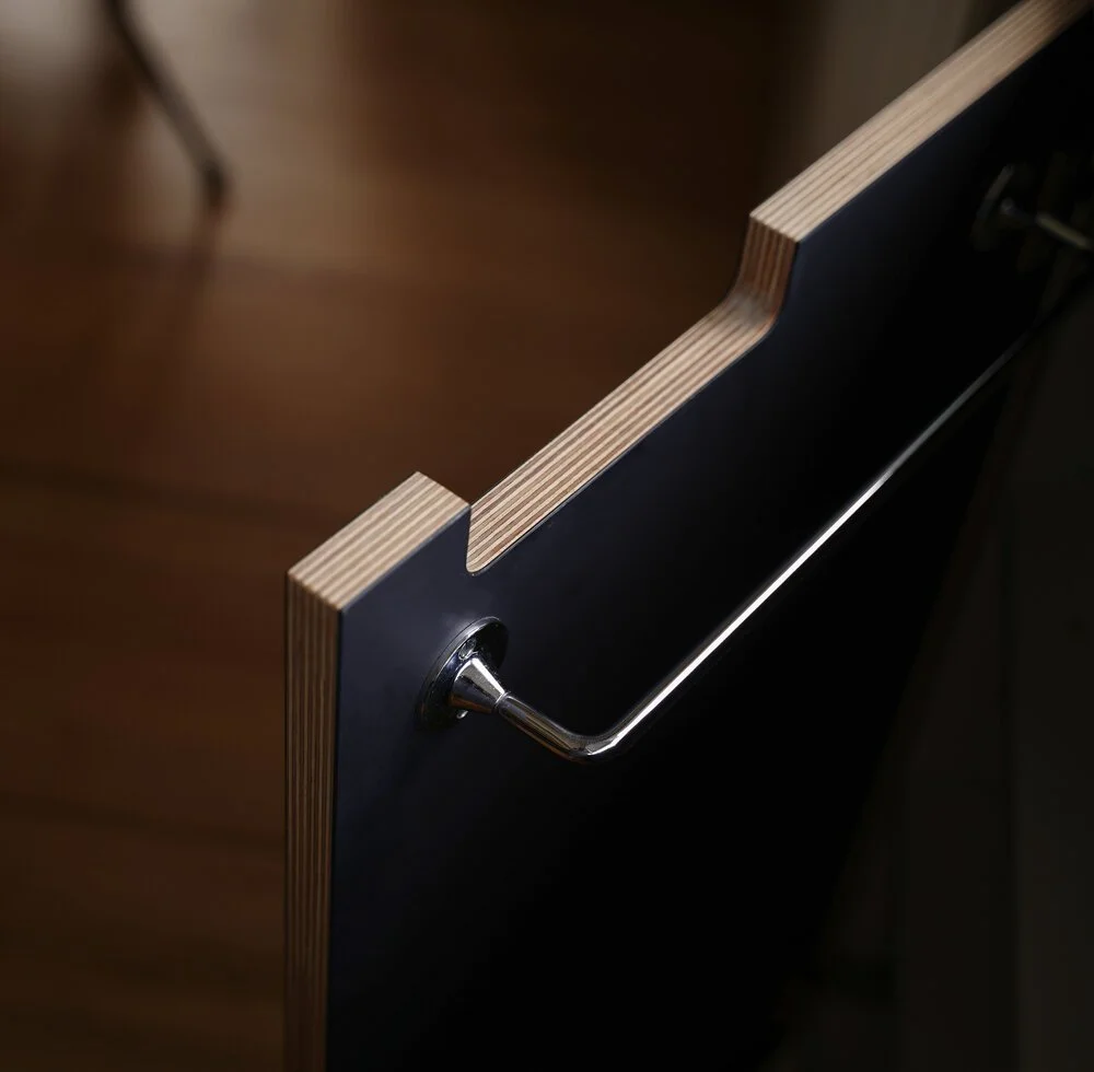 Close-up of a dark-colored foldable table with a wooden edge and a metal handle on a wooden floor.