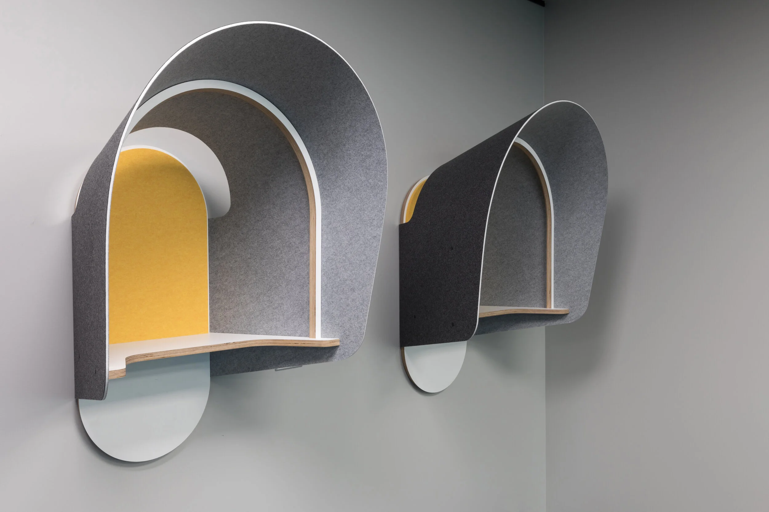 Two modern, wall-mounted, arch-shaped shelves with curved sides and a yellow interior, each with a white circular base, on a light gray wall.