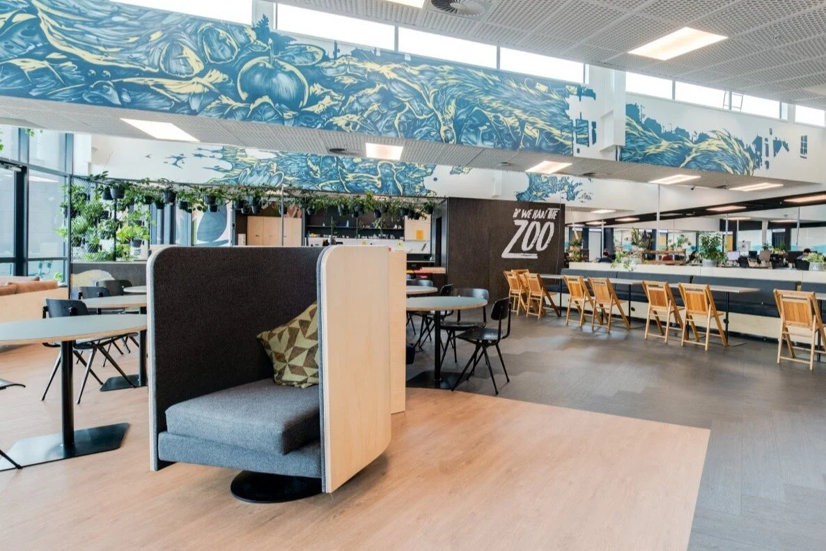Modern interior of a zoo cafe or restaurant with tables, chairs, and a chalkboard sign that reads "We Run the Zoo."