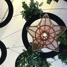 A decorative star-shaped lantern made of woven material hanging above black circular patterns and green plants on a tiled floor.