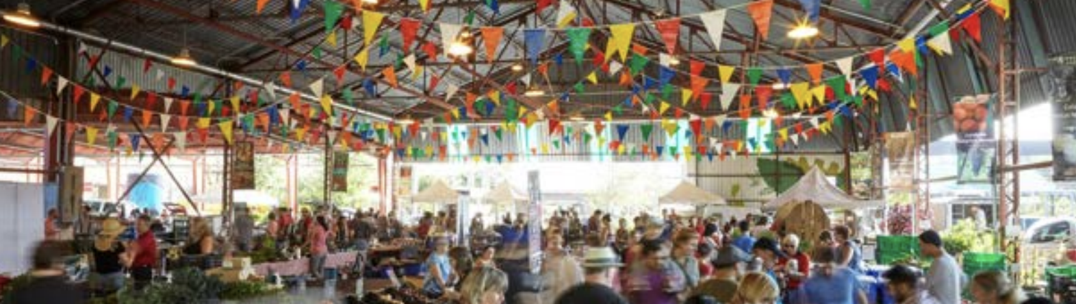 Indoor market or festival with many people and colorful bunting flags hanging from the ceiling.