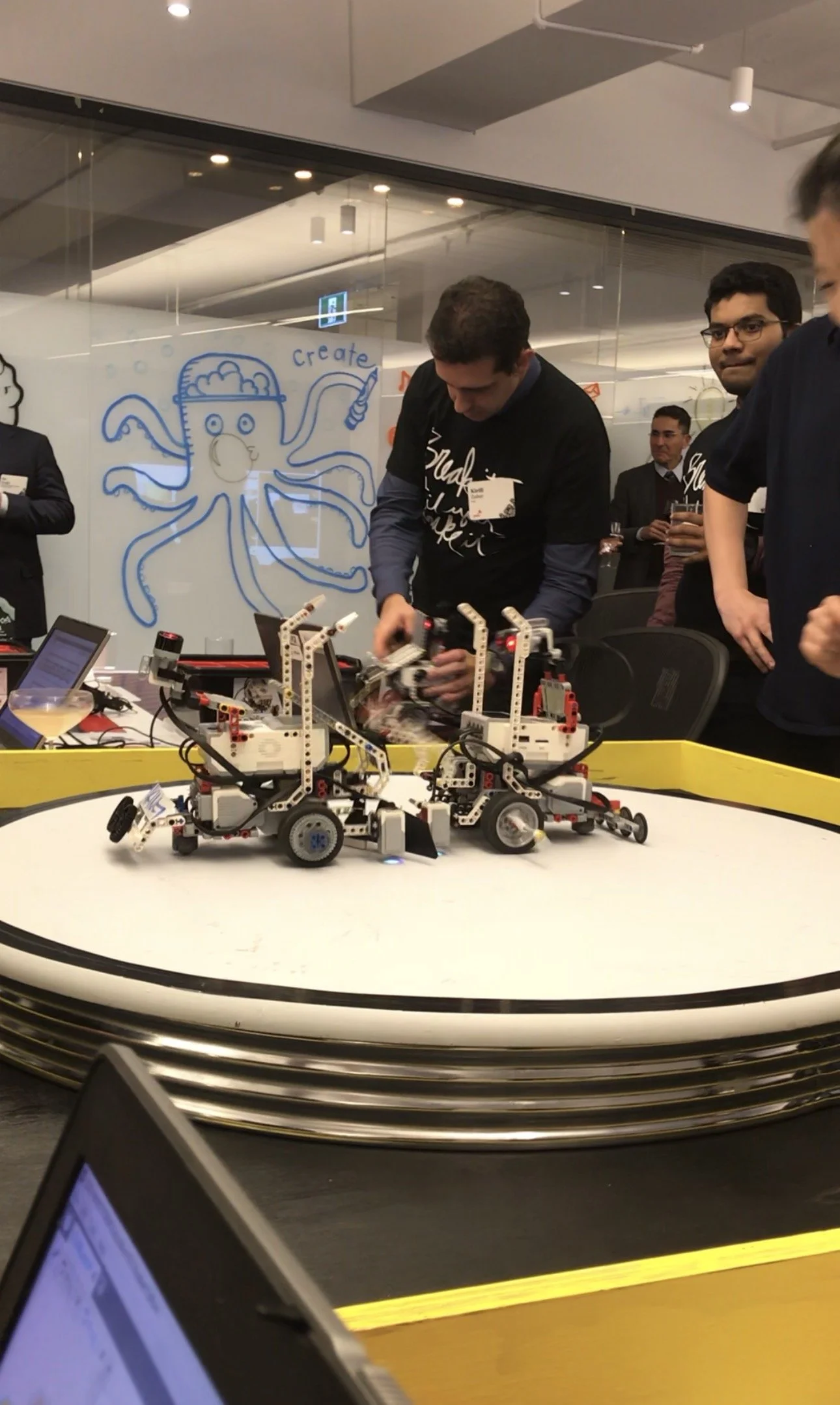 People operating Lego Mindstorms robots around a circular arena during a robotics competition or demonstration.