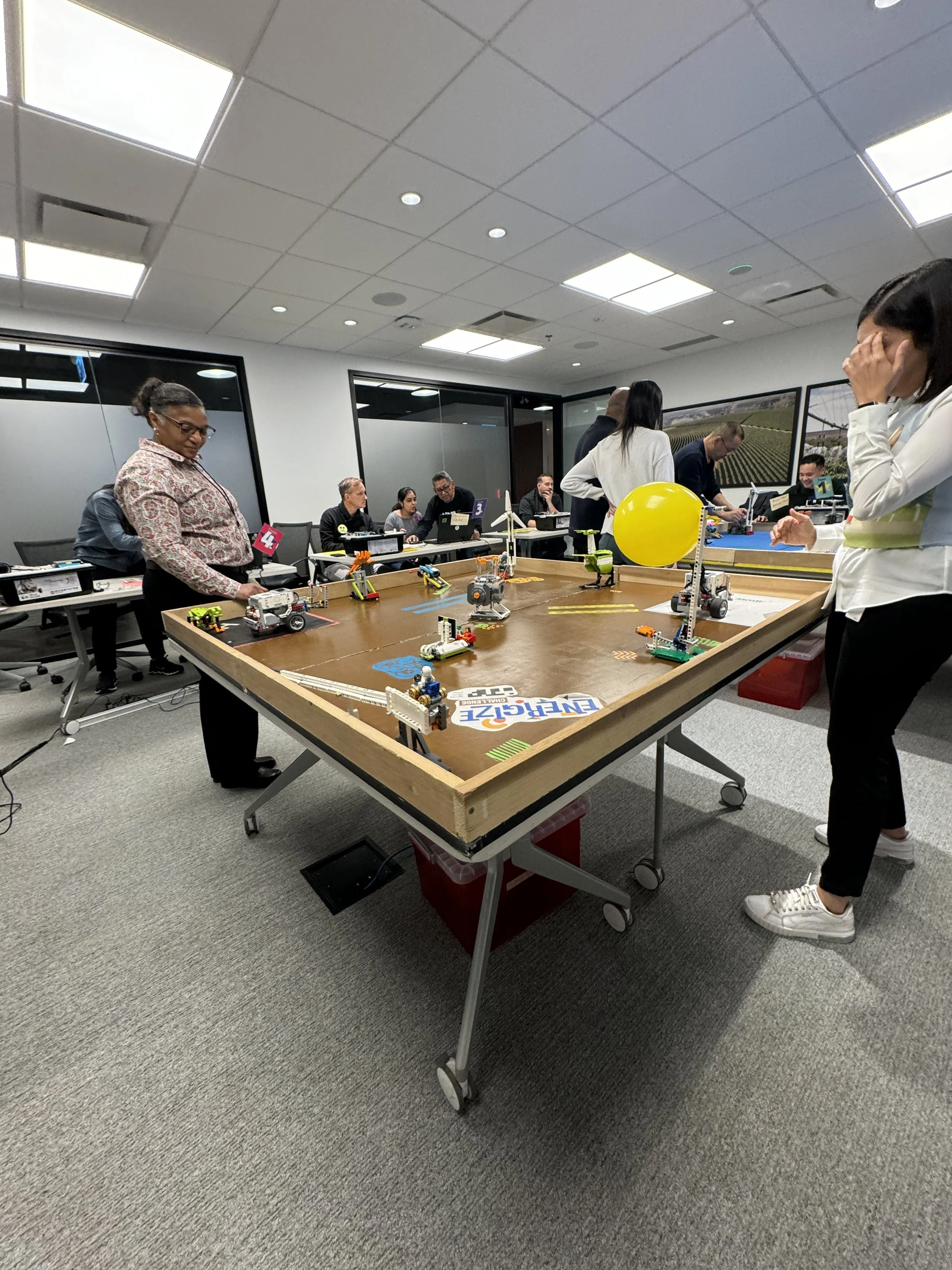 People playing a robotics game on a large table in an office conference room.