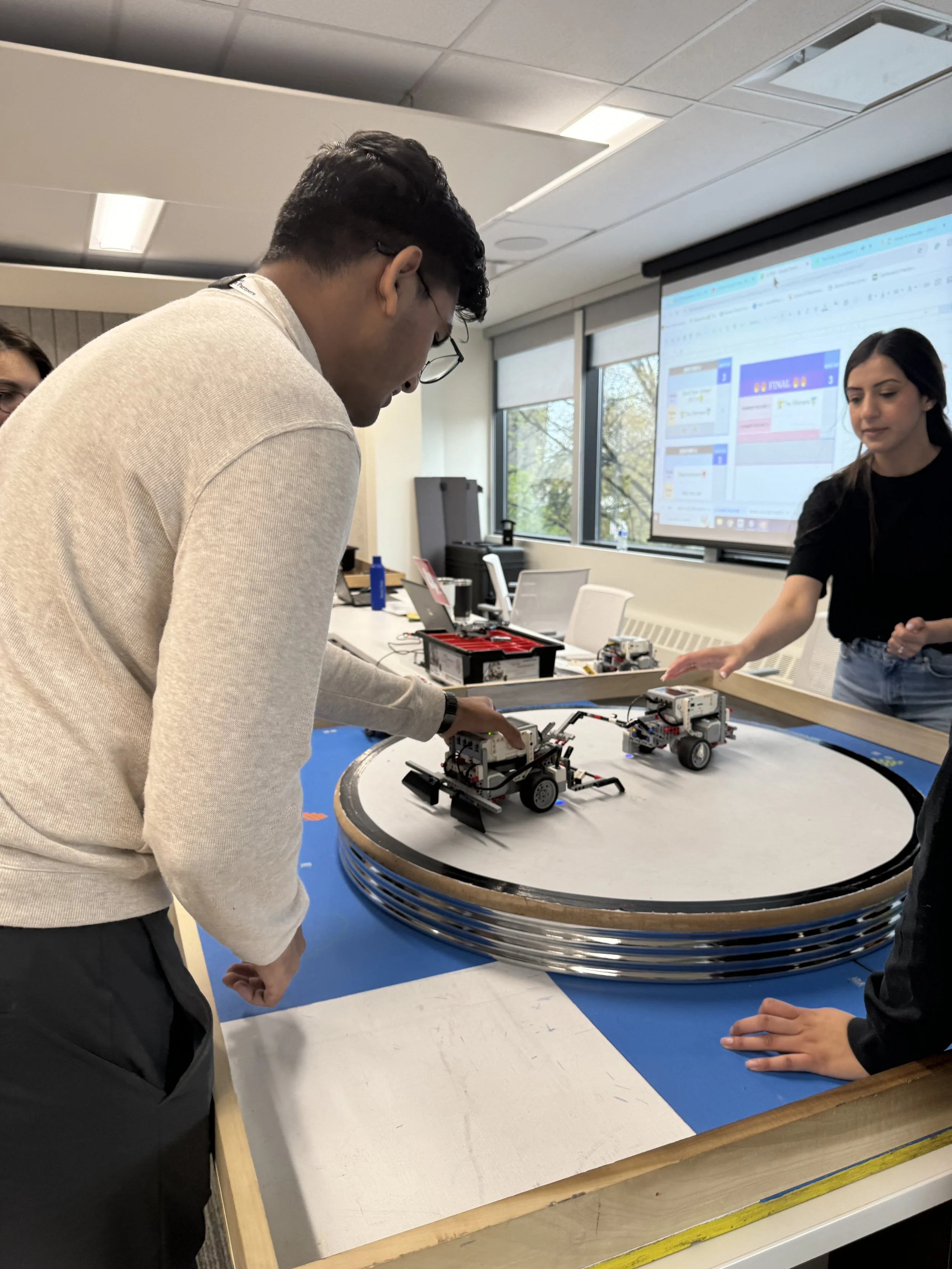 Students working with robotics on a circular track in a classroom.