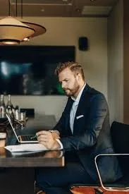 A man in a suit working on a laptop at a restaurant or cafe table.