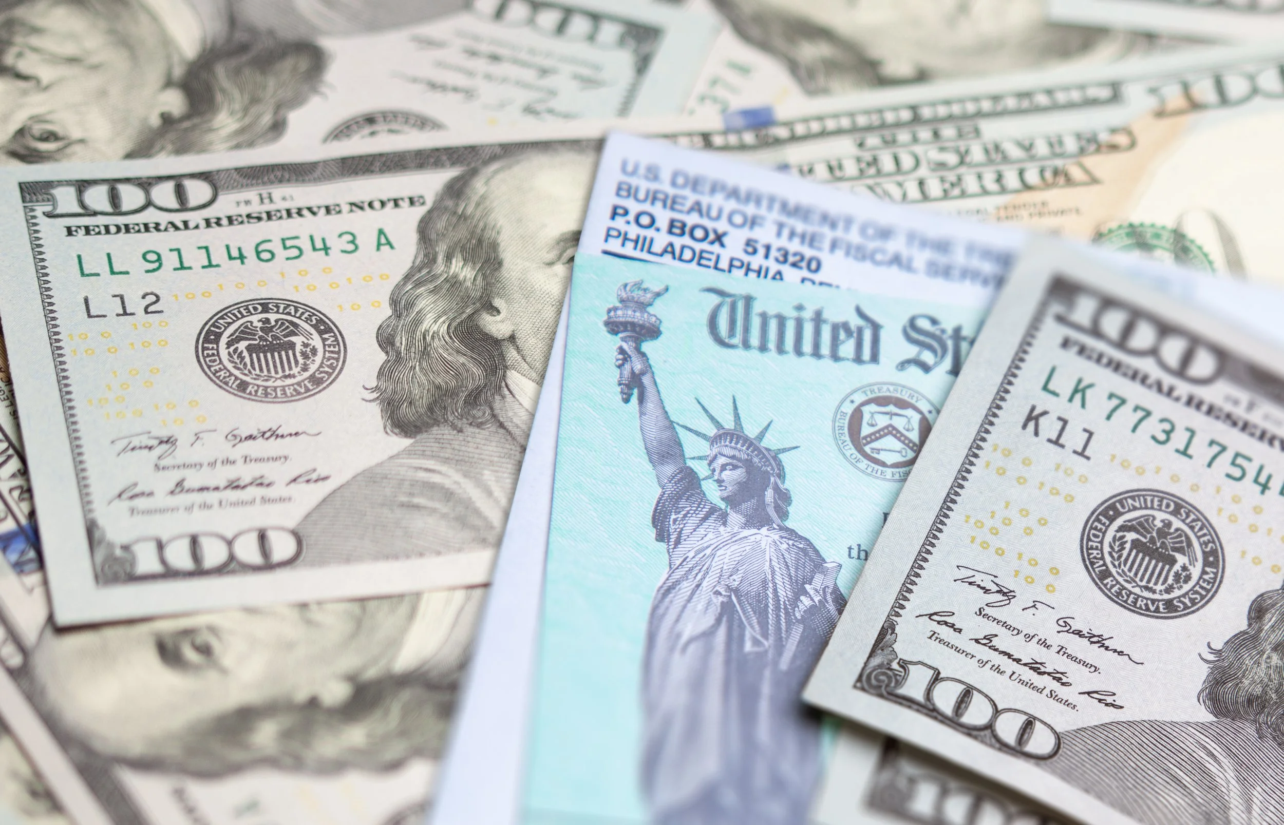 Various U.S. currency including one hundred dollar bills and a hundred dollar bill with the image of Benjamin Franklin, along with a blue U.S. Postal Service money order and a United States Postal Service money order.