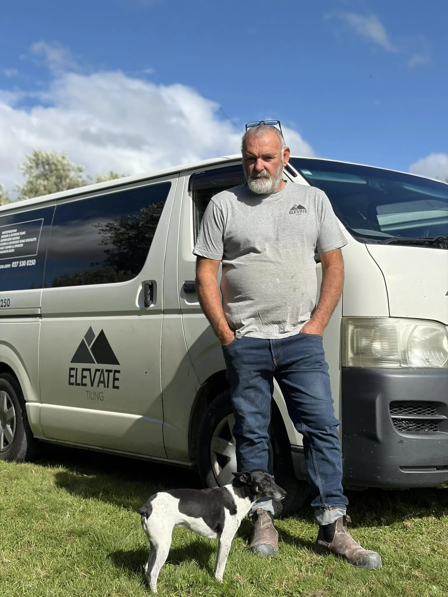A middle-aged man with dark, slicked-back hair sitting on a cushioned bench against a plain wall, looking to his left.