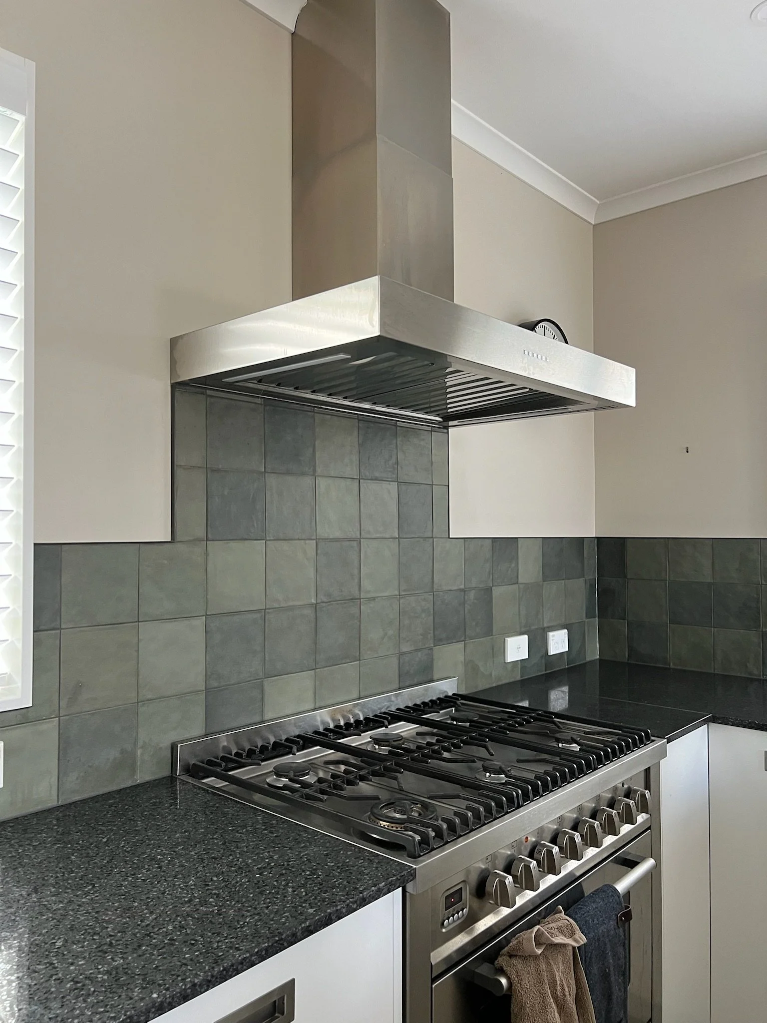 A modern kitchen with a stainless steel range hood, a gas stove with multiple burners, gray tiled backsplash, and black granite countertops.